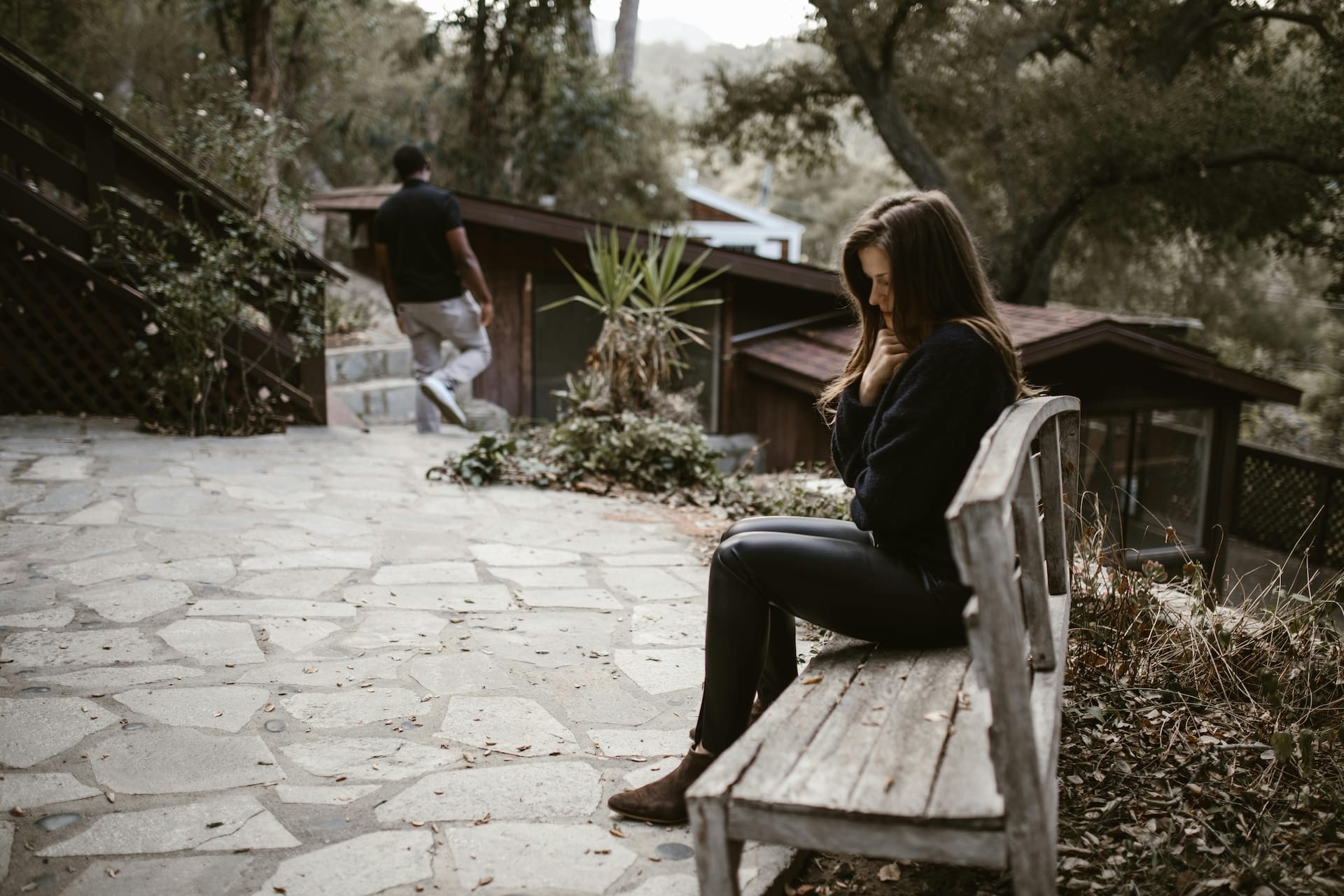 A woman in despair seated on a bench with a man walking away from her